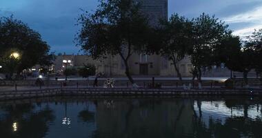 The drone flies over the surface of the pool water near the ancient complex Ulugbek Madrasah at night. Old Bukhara, Uzbekistan. video