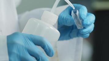 A laboratory technician in a white coat and protective gloves pours liquid into a chemical dish. video