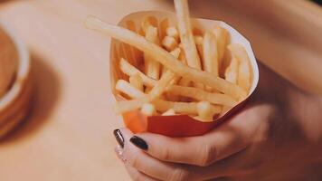 avvicinamento Immagine di un' donna Tenere e mangiare francese patatine fritte e Hamburger con fritte pollo su il tavolo a casa video