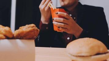 avvicinamento Immagine di un' donna Tenere e mangiare francese patatine fritte e Hamburger con fritte pollo su il tavolo a casa video