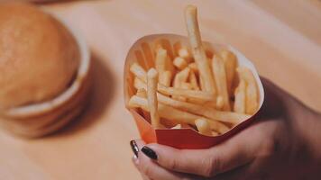 Closeup image of a woman holding and eating french fries and hamburger with fried chicken on the table at home video