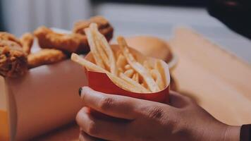 Closeup image of a woman holding and eating french fries and hamburger with fried chicken on the table at home video