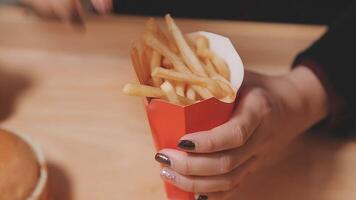 avvicinamento Immagine di un' donna Tenere e mangiare francese patatine fritte e Hamburger con fritte pollo su il tavolo a casa video