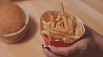 avvicinamento Immagine di un' donna Tenere e mangiare francese patatine fritte e Hamburger con fritte pollo su il tavolo a casa video