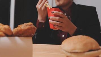 avvicinamento Immagine di un' donna Tenere e mangiare francese patatine fritte e Hamburger con fritte pollo su il tavolo a casa video