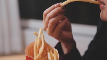 Closeup image of a woman holding and eating french fries and hamburger with fried chicken on the table at home video