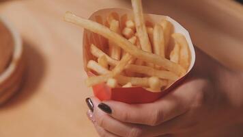 avvicinamento Immagine di un' donna Tenere e mangiare francese patatine fritte e Hamburger con fritte pollo su il tavolo a casa video