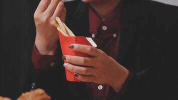 Closeup image of a woman holding and eating french fries and hamburger with fried chicken on the table at home video