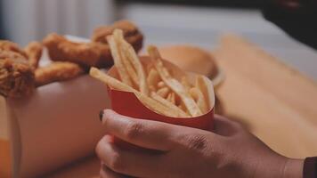 Closeup image of a woman holding and eating french fries and hamburger with fried chicken on the table at home video