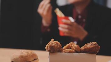 avvicinamento Immagine di un' donna Tenere e mangiare francese patatine fritte e Hamburger con fritte pollo su il tavolo a casa video