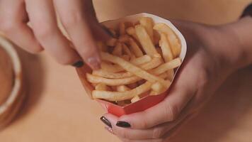 avvicinamento Immagine di un' donna Tenere e mangiare francese patatine fritte e Hamburger con fritte pollo su il tavolo a casa video