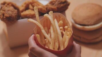 avvicinamento Immagine di un' donna Tenere e mangiare francese patatine fritte e Hamburger con fritte pollo su il tavolo a casa video