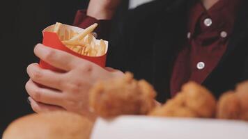 avvicinamento Immagine di un' donna Tenere e mangiare francese patatine fritte e Hamburger con fritte pollo su il tavolo a casa video