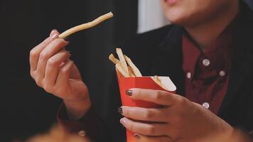 fermer image de une femme en portant et en mangeant français frites et Hamburger avec frit poulet sur le table à Accueil video