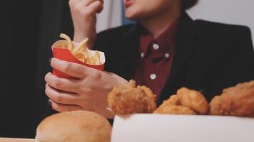 fermer image de une femme en portant et en mangeant français frites et Hamburger avec frit poulet sur le table à Accueil video