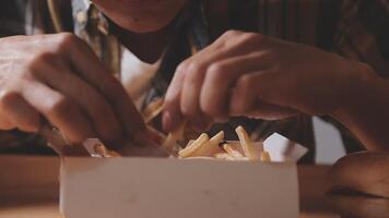 Closeup image of a woman holding and eating french fries and hamburger with fried chicken on the table at home video