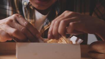 närbild bild av en kvinna innehav och äter franska frites och hamburgare med friterad kyckling på de tabell på Hem video