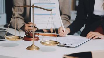 Business and lawyers discussing contract papers with brass scale on desk in office. Law, legal services, advice, justice and law concept picture with film grain effect video