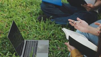 Group of happy young Asian college students sitting on a bench, looking at a laptop screen, discussing and brainstorming on their school project together. video