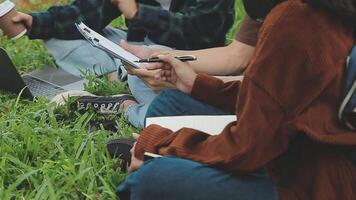 Group of happy young Asian college students sitting on a bench, looking at a laptop screen, discussing and brainstorming on their school project together. video