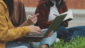 grupp av Lycklig ung asiatisk högskola studenter Sammanträde på en bänk, ser på en bärbar dator skärm, diskuterar och brainstorming på deras skola projekt tillsammans. video