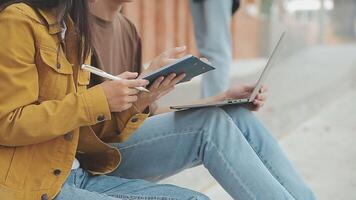 Group of happy young Asian college students sitting on a bench, looking at a laptop screen, discussing and brainstorming on their school project together. video