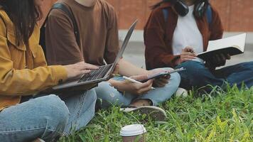 grupo de contento joven asiático Universidad estudiantes sentado en un banco, mirando a un ordenador portátil pantalla, que se discute y lluvia de ideas en su colegio proyecto juntos. video