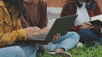 grupo do feliz jovem ásia Faculdade alunos sentado em uma banco, olhando às uma computador portátil tela, discutindo e debate em seus escola projeto junto. video