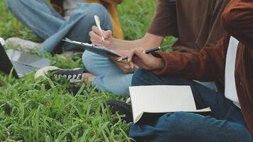 gruppo di contento giovane asiatico Università studenti seduta su un' panca, guardare a un' il computer portatile schermo, discutere e di brainstorming su loro scuola progetto insieme. video