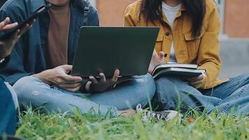 Gruppe von glücklich jung asiatisch Hochschule Studenten Sitzung auf ein Bank, suchen beim ein Laptop Bildschirm, diskutieren und Brainstorming auf ihr Schule Projekt zusammen. video