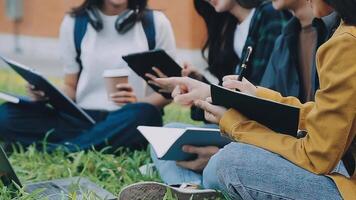 grupo do feliz jovem ásia Faculdade alunos sentado em uma banco, olhando às uma computador portátil tela, discutindo e debate em seus escola projeto junto. video