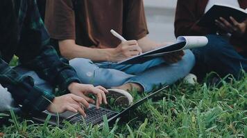 Group of happy young Asian college students sitting on a bench, looking at a laptop screen, discussing and brainstorming on their school project together. video