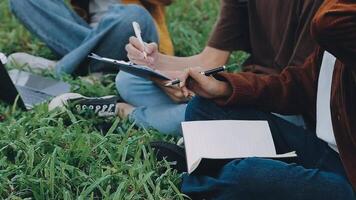 Gruppe von glücklich jung asiatisch Hochschule Studenten Sitzung auf ein Bank, suchen beim ein Laptop Bildschirm, diskutieren und Brainstorming auf ihr Schule Projekt zusammen. video