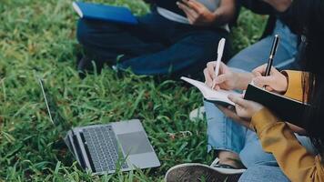 Group of happy young Asian college students sitting on a bench, looking at a laptop screen, discussing and brainstorming on their school project together. video