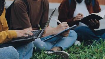 Gruppe von glücklich jung asiatisch Hochschule Studenten Sitzung auf ein Bank, suchen beim ein Laptop Bildschirm, diskutieren und Brainstorming auf ihr Schule Projekt zusammen. video