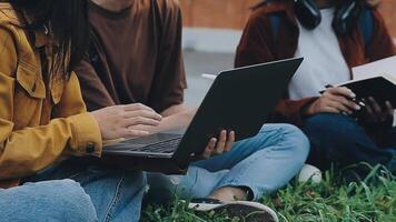 grupo do feliz jovem ásia Faculdade alunos sentado em uma banco, olhando às uma computador portátil tela, discutindo e debate em seus escola projeto junto. video