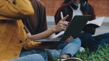 Group of happy young Asian college students sitting on a bench, looking at a laptop screen, discussing and brainstorming on their school project together. video