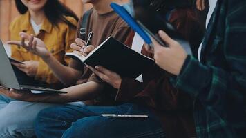 grupo do feliz jovem ásia Faculdade alunos sentado em uma banco, olhando às uma computador portátil tela, discutindo e debate em seus escola projeto junto. video