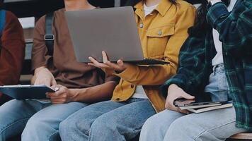 grupo do feliz jovem ásia Faculdade alunos sentado em uma banco, olhando às uma computador portátil tela, discutindo e debate em seus escola projeto junto. video