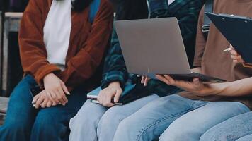 grupp av Lycklig ung asiatisk högskola studenter Sammanträde på en bänk, ser på en bärbar dator skärm, diskuterar och brainstorming på deras skola projekt tillsammans. video