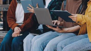 Gruppe von glücklich jung asiatisch Hochschule Studenten Sitzung auf ein Bank, suchen beim ein Laptop Bildschirm, diskutieren und Brainstorming auf ihr Schule Projekt zusammen. video