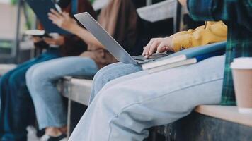 Group of happy young Asian college students sitting on a bench, looking at a laptop screen, discussing and brainstorming on their school project together. video