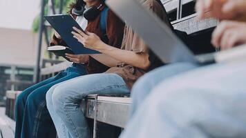 grupp av Lycklig ung asiatisk högskola studenter Sammanträde på en bänk, ser på en bärbar dator skärm, diskuterar och brainstorming på deras skola projekt tillsammans. video