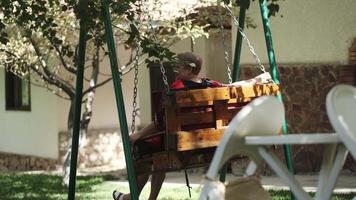 Adult woman swinging on a swing in the yard of her house video