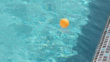 un naranja pelota flotadores en el olas en un al aire libre privado piscina. un soleado verano día. video