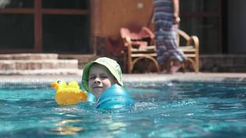 Little boy in panama swims with inflatable toys in the pool on a sunny day video