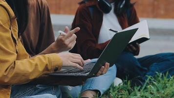 grupo do feliz jovem ásia Faculdade alunos sentado em uma banco, olhando às uma computador portátil tela, discutindo e debate em seus escola projeto junto. video