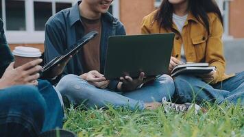 Group of happy young Asian college students sitting on a bench, looking at a laptop screen, discussing and brainstorming on their school project together. video