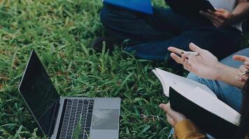 Group of happy young Asian college students sitting on a bench, looking at a laptop screen, discussing and brainstorming on their school project together. video