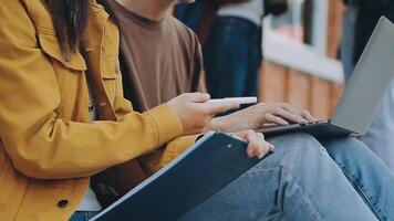 Group of happy young Asian college students sitting on a bench, looking at a laptop screen, discussing and brainstorming on their school project together. video